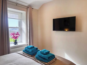 A hotel room with a bed, a window with curtains, a TV mounted on the wall, and a view of the outside.