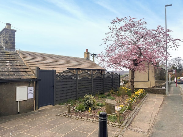 A traditional stone cottage with a tiled roof, a wooden gate, and a flowering tree.