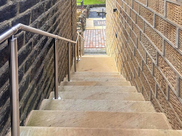 A staircase with stone steps and metal railings, leading to a brick wall.