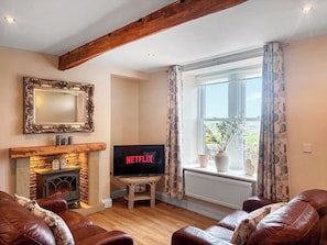 A living room with a fireplace, a television, leather sofas, and a large window with curtains.