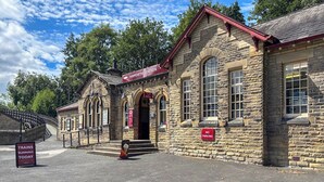 Un edificio storico in pietra con tetto rosso, con la scritta 'Haworth Station' e un cartello 'Divieto di parcheggio'.