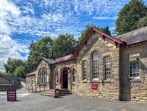 Un edificio histórico de piedra con techo rojo, con la leyenda 'Haworth Station' y un cartel de 'Prohibido Estacionar'.