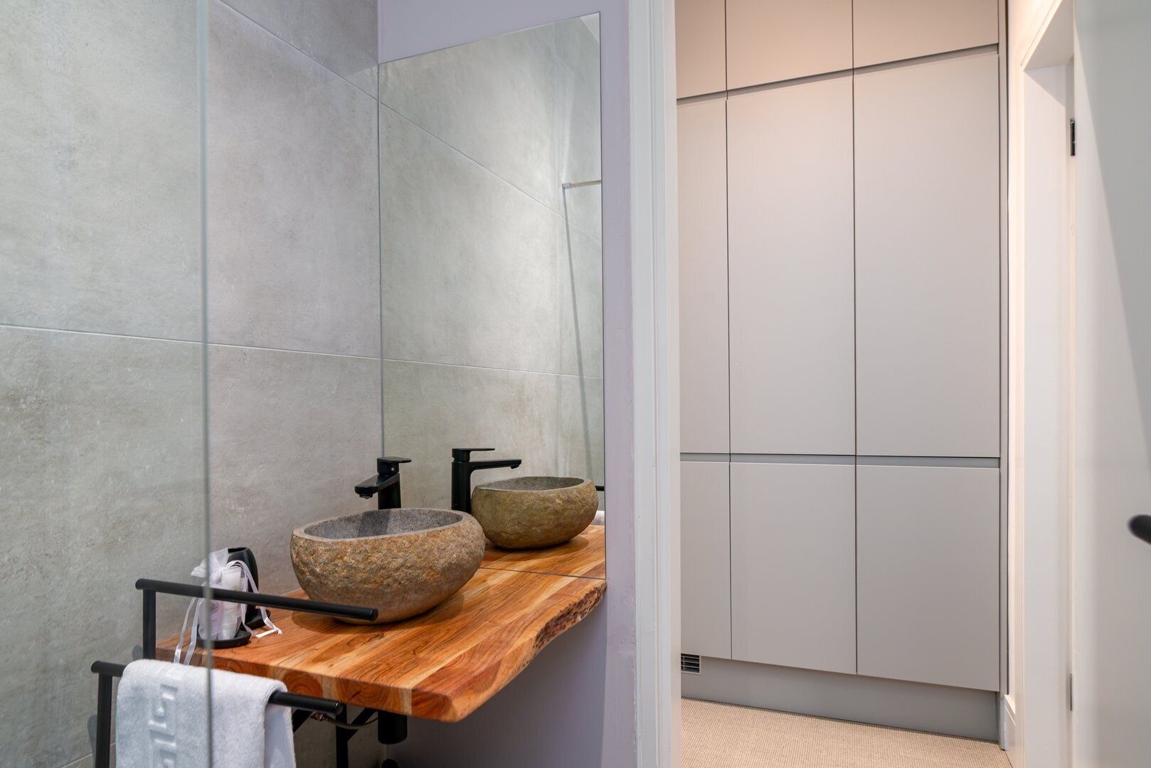 Une salle de bain moderne avec un meuble-lavabo en bois, deux vasques en pierre et un grand miroir.
