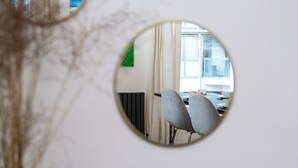 Un espejo redondo que refleja una habitación con una ventana, un radiador y dos sillas.