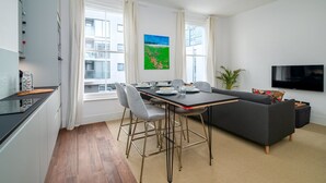Un apartamento moderno con comedor, sofá, televisor y ventana con cortinas.