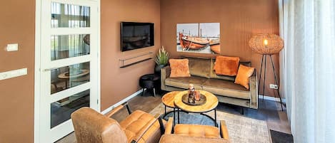 A modern living room with a sofa, two armchairs, a coffee table, a TV, and a large window with curtains.