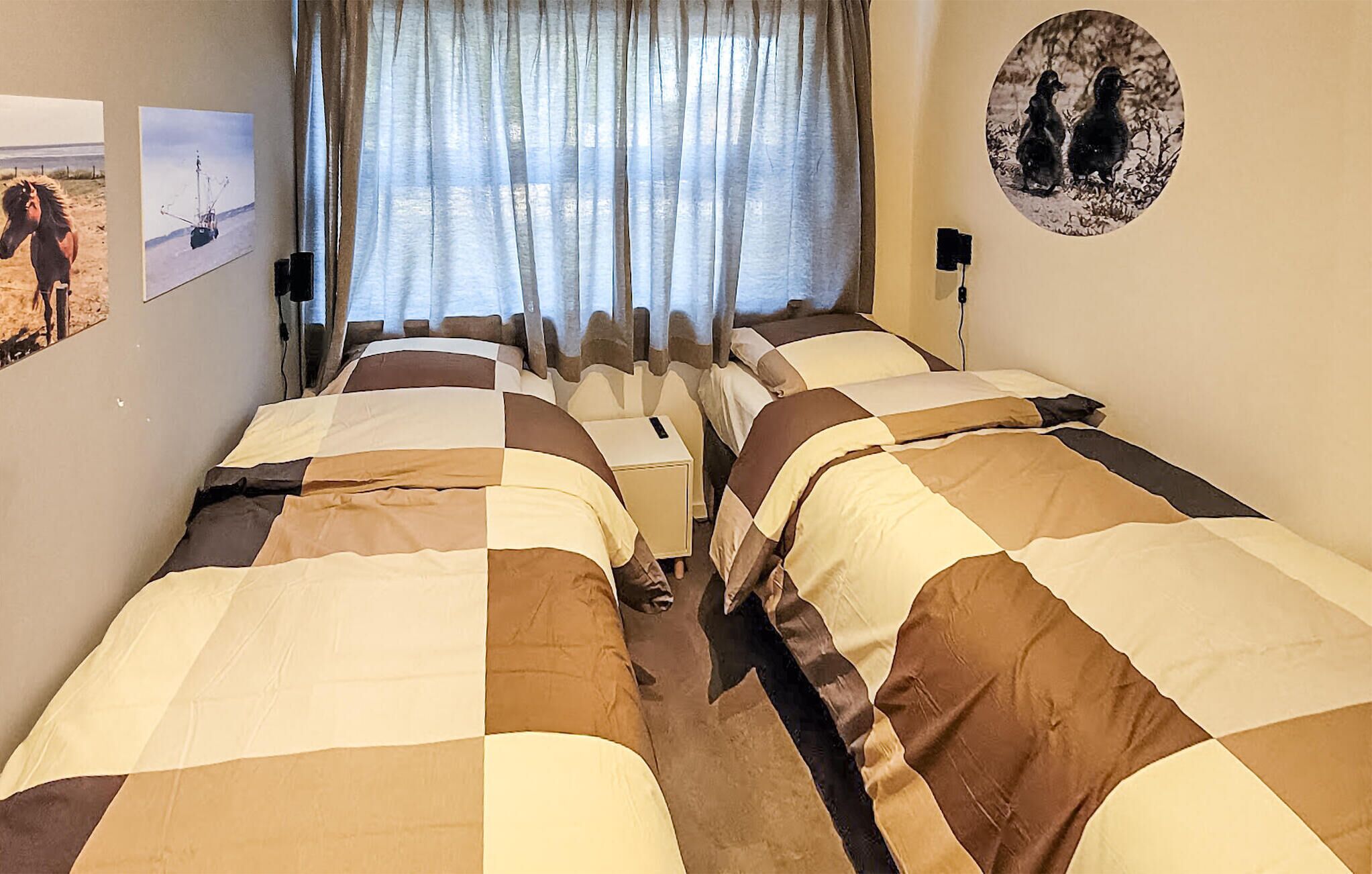 Une chambre avec deux lits, une fenêtre avec des rideaux et des œuvres d’art murales.