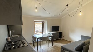 A modern kitchen with a gas stove, a red and white kettle, and a dining area with a table and chairs. There is a TV and a sofa in the living area. - San Donato residence (Montepulciano)