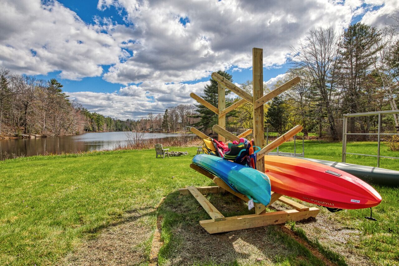 Un portarimorchi per kayak con due kayak, una panca e una sedia vicino a un lago.