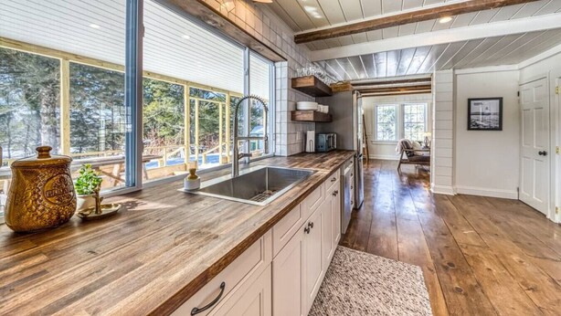 Un'ampia cucina con un'isola grande, pavimento in legno e vista sull'esterno tramite ampie finestre.