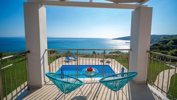 Un balcón con piscina, dos sillas y una mesa con un objeto rojo.