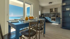 Una cocina moderna con vista al mar, un comedor con sillas y una mesa, y una pared de acento azul.