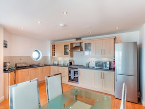 A modern kitchen with wooden cabinets, stainless steel appliances, and a glass dining table.
