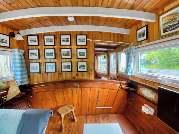 Une cabane aux murs en bois, ornée de quelques tableaux, avec un petit tabouret et une fenêtre donnant sur un paysage verdoyant.