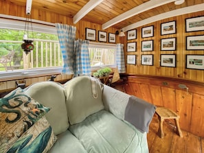 A cozy room with a wooden ceiling, a sofa with patterned cushions, a small stool, and framed pictures on the wall.