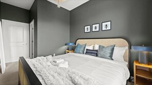 Een slaapkamer met een bed, een zachte, witte deken en kussens. Er hangen kunstwerken boven het bed.