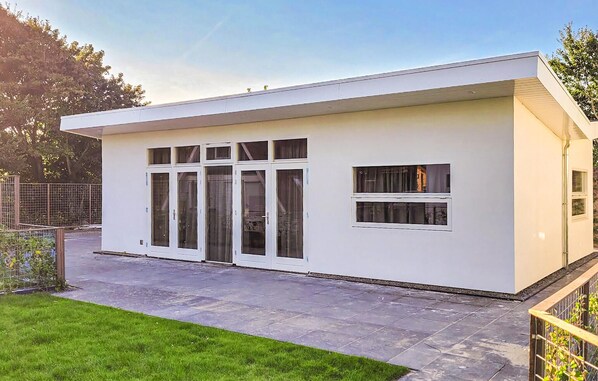 A modern, single-story building with large glass doors and windows, a flat roof, and a paved patio area. - Beautiful home in Den Oever with WiFi (Den Oever)