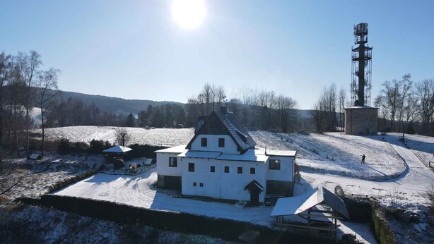 Un bâtiment blanc, doté d’un toit à forte pente, entouré de champs et d’arbres recouverts de neige.
