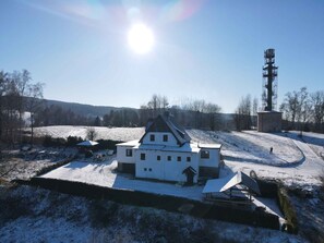 A white building with a steep roof, surrounded by snow-covered fields and trees.