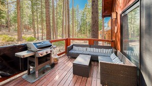 Una terraza con una parrilla, mobiliario de mimbre y vistas a un bosque.