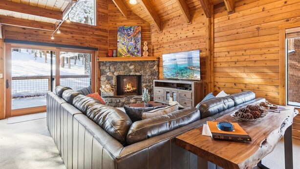 Un interior acogedor de cabaña con chimenea de piedra, asientos de cuero y un televisor grande.