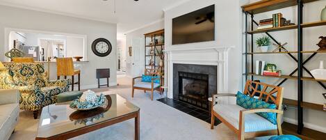 A living room with a fireplace, a ceiling fan, a clock, and a bookshelf.