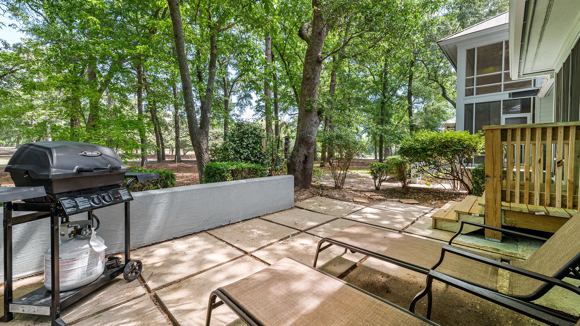 Un patio con una parrilla, una terraza de madera y una casa al fondo.
