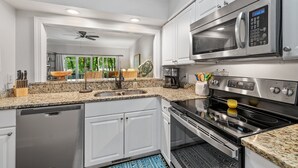 A modern kitchen with white cabinetry, a stainless steel microwave, a built-in oven, a dishwasher, and a granite countertop. - 3BR/3BA Ground Level ,Gated Pawleys Plantation (Pawleys Island)