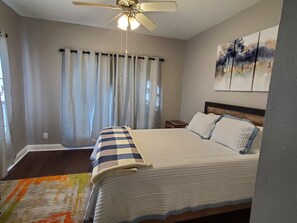 A bedroom with a bed, a ceiling fan, a nightstand, and a painting on the wall.