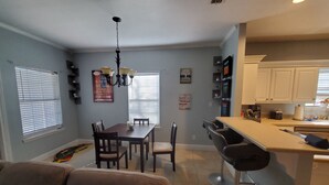 Un comedor con mesa y sillas, una barra con taburetes y una zona de cocina con armarios y electrodomésticos.