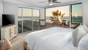 Un dormitorio con una cama grande, televisión y balcón con vista a la playa y al océano.