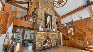 A spacious living area with a stone fireplace, wooden staircase, and a large wooden ceiling beam. - Private Retreat with Majestic Views - Just 15 Minutes from Branson (Saddlebrooke(Chestnutridge))