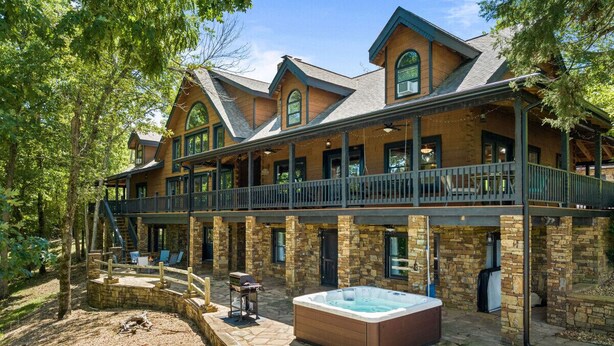 A large, multi-story lodge with a stone exterior, a hot tub, and a covered deck area. - Private Retreat with Majestic Views - Just 15 Minutes from Branson (Saddlebrooke(Chestnutridge))