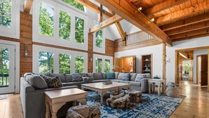 A spacious living room with a large sectional sofa, a coffee table, and a patterned rug. There are large windows allowing natural light and views of greenery outside. - Private Retreat with Majestic Views - Just 15 Minutes from Branson (Saddlebrooke(Chestnutridge))