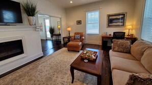A living room with a fireplace, a sofa, a coffee table with decorative items, a television, and a ceiling fan. - Woods Hollow - Upscale renovated home, minutes to All-Star Village (Laurens)