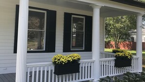 A white house with black shutters, a porch with white railings, and two flower boxes with yellow flowers. - Woods Hollow - Upscale renovated home, minutes to All-Star Village (Laurens)