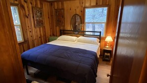 Een slaapkamer met houten lambrisering, een bed, een bedlamp, een raam en een deur.
