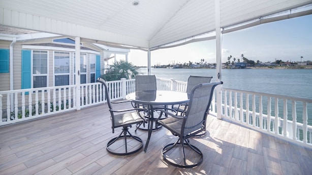 A covered outdoor area with a table and chairs, a view of the water, and a white railing. - Coastal Breeze - Waterfront, Pools, Golf, Tennis (Port Isabel)