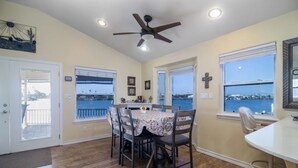 A dining area with a table, chairs, a ceiling fan, and windows with a view. - Coastal Breeze - Waterfront, Pools, Golf, Tennis (Port Isabel)