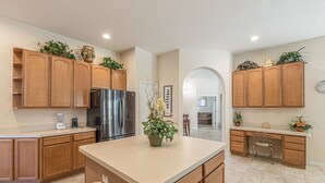 A modern kitchen with wooden cabinets, a stainless steel refrigerator, and a central island with a potted plant. - Large executive 4 Bed Villa w/pool & spa, set in peaceful community. Near WDW (Davenport)