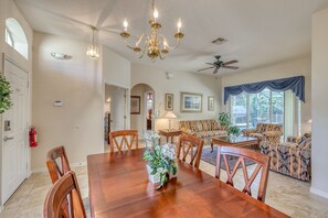 A spacious dining area with a wooden table and chairs, a chandelier, and a ceiling fan.