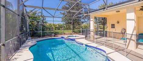 A swimming pool with a glass enclosure, surrounded by a patio area with seating and a covered section.