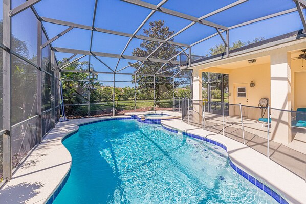 A swimming pool with a glass enclosure, surrounded by a patio area with seating and a covered section.