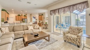 A spacious living room with a sofa, armchair, and coffee table. There is a kitchen in the background with wooden cabinets and a dining area. - Large executive 4 Bed Villa w/pool & spa, set in peaceful community. Near WDW (Davenport)