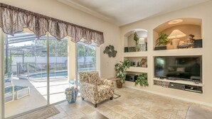 A spacious living room with a large TV, comfortable seating, a pool view, and a well-organized entertainment shelf. - Large executive 4 Bed Villa w/pool & spa, set in peaceful community. Near WDW (Davenport)