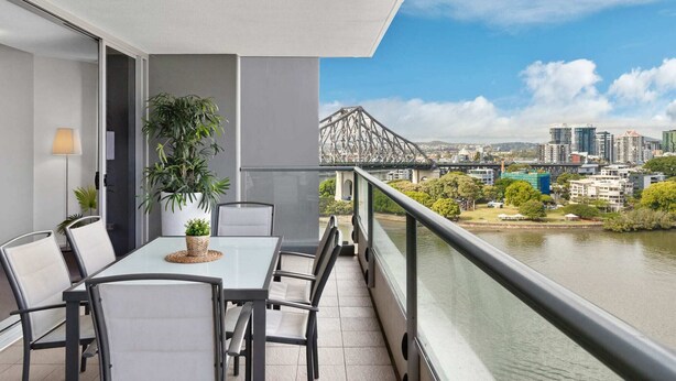 Ein Balkon mit Tisch und Stühlen, einem Blumentopf und Blick auf eine Brücke sowie Stadtansicht.