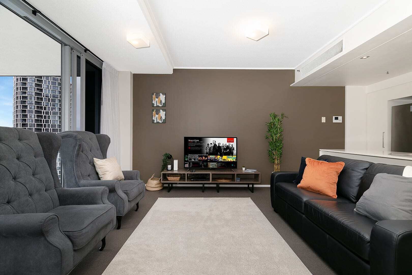 A modern living room with a large flat-screen TV, grey sofas, and a minimalist design.