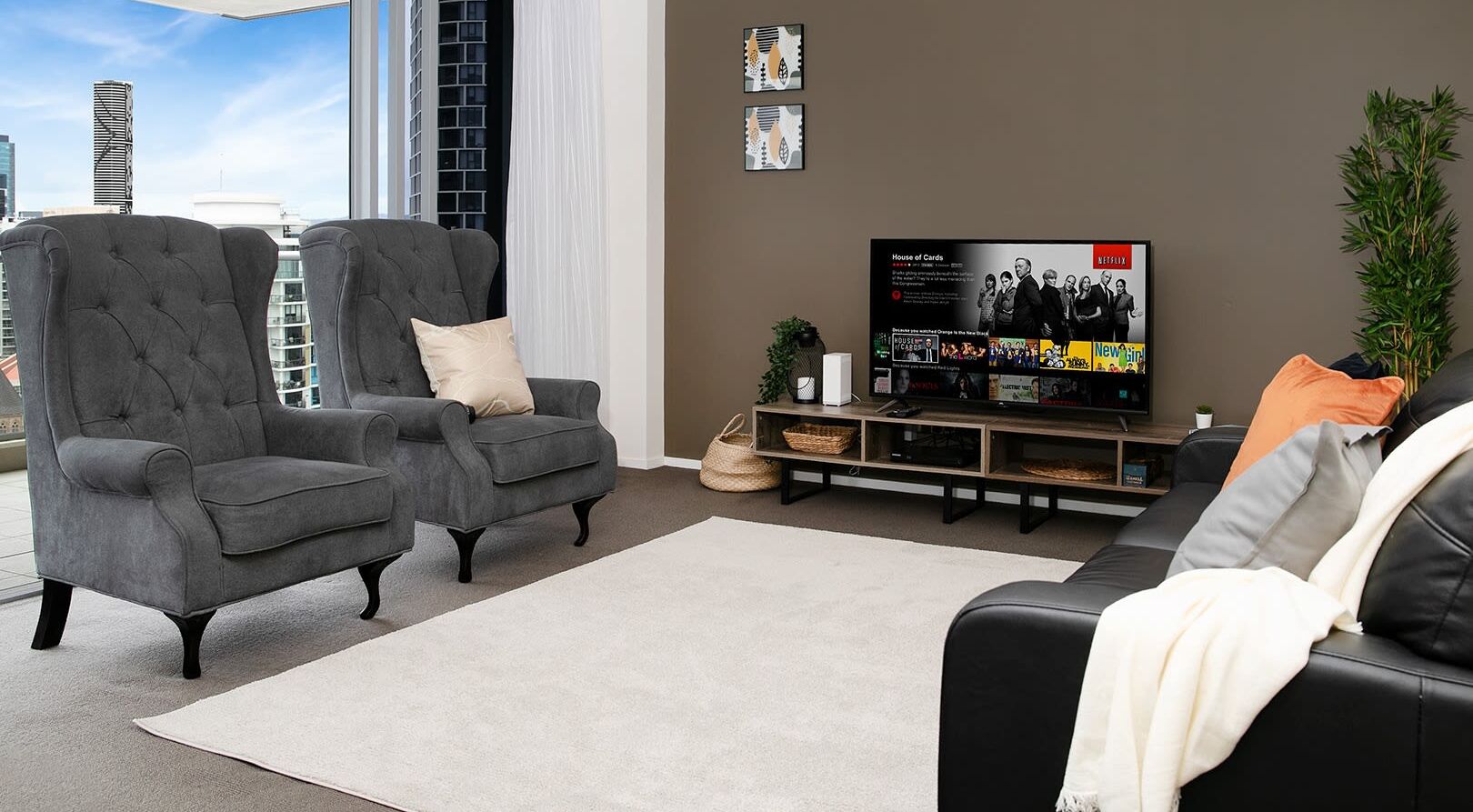 Uma sala moderna com duas poltronas cinzentas, um sofá preto e uma televisão de tela plana grande.
