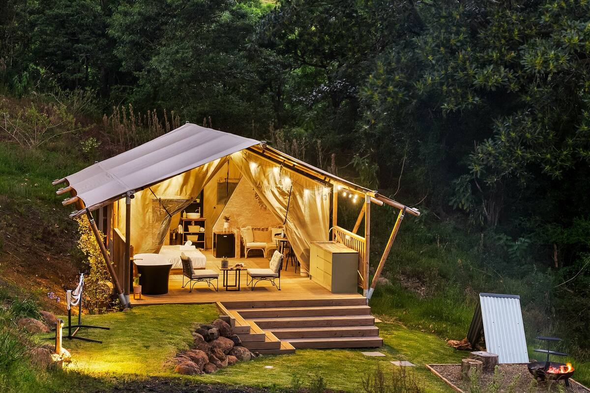 Alojamiento en tienda de campaña con terraza de madera, zona de estar al aire libre y una chimenea.
