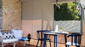 A covered outdoor seating area with a table and chairs, a cushioned bench, and a small potted plant. - Cicada Luxury Camping (Jerrara)